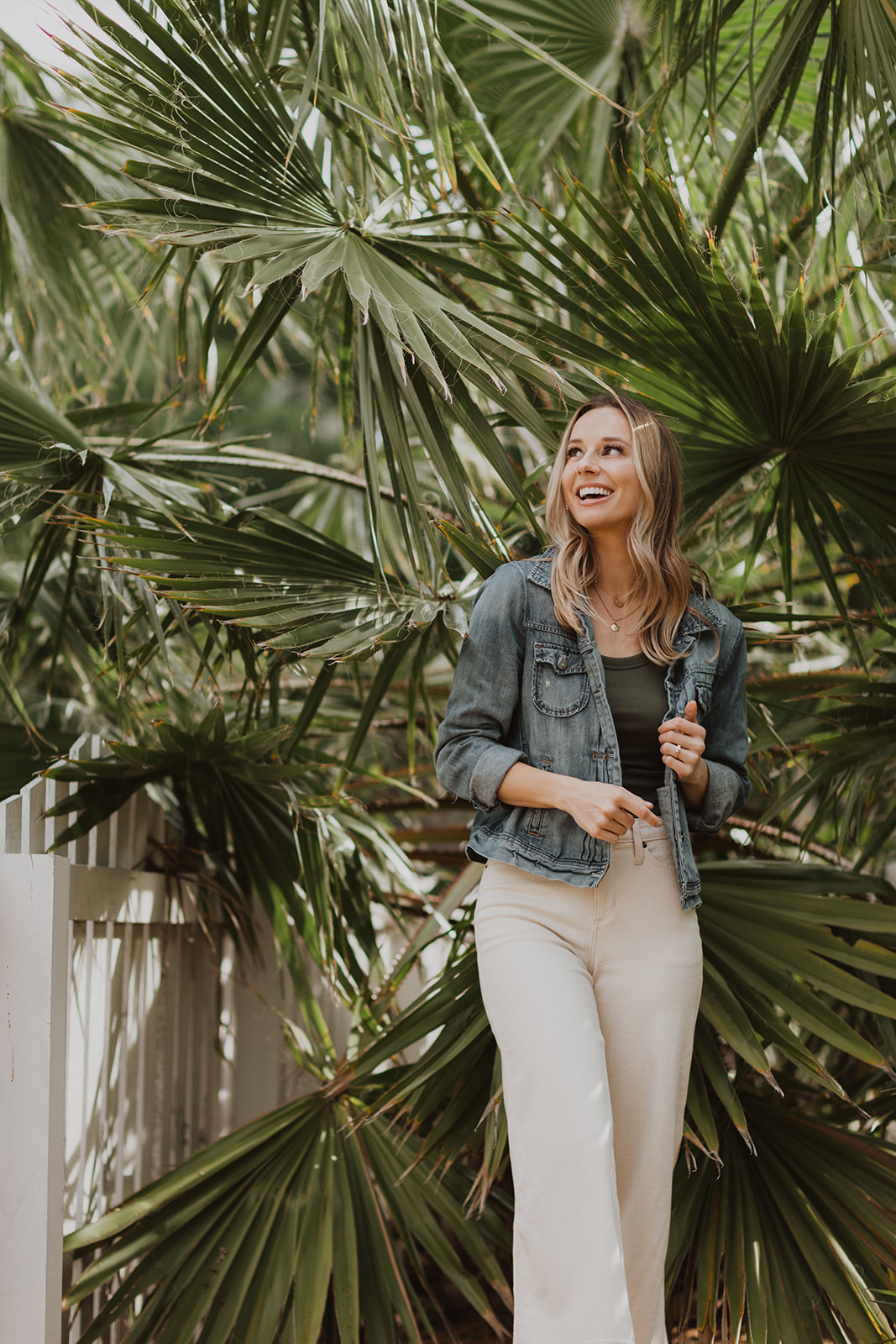 woman standing under saw palmetto tree in denim jacket and white high rise sailor pants